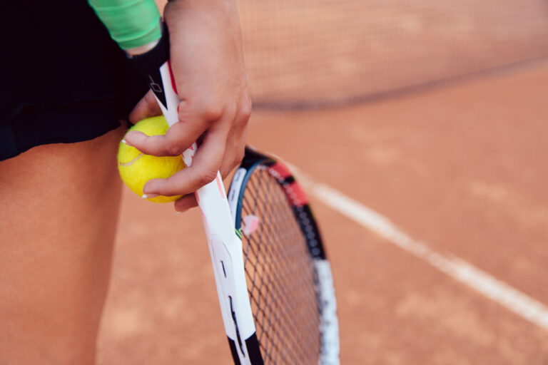 Woman holding tennis racket and ball on clay court. Close-up. Sport concept.